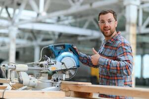A carpenter works on woodworking the machine tool. Man collects furniture boxes. Saws furniture details with a circular saw. Process of sawing parts in parts. Against the background of the workshop. photo
