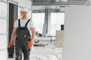 Portrait of a builder in working uniform with protective helmet standing with instruments at the construction site indoors photo