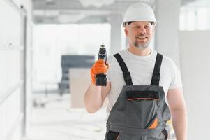 Portrait of a builder in working uniform with protective helmet standing with instruments at the construction site indoors photo
