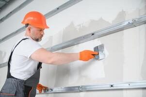 man drywall worker using trowel for plasterer putting stucco on plasterboard white wall. photo