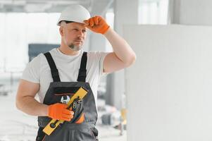 Portrait of a builder in working uniform with protective helmet standing with instruments at the construction site indoors photo