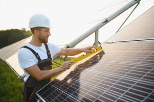 Side view of male worker installing solar modules and support structures of photovoltaic solar array. Electrician wearing safety helmet while working with solar panel. Concept of sun energy photo