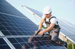 Side view of male worker installing solar modules and support structures of photovoltaic solar array. Electrician wearing safety helmet while working with solar panel. Concept of sun energy photo