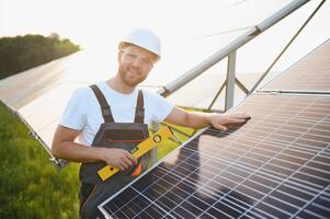 Side view of male worker installing solar modules and support structures of photovoltaic solar array. Electrician wearing safety helmet while working with solar panel. Concept of sun energy photo