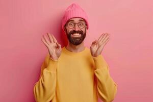 Playful bearded man in colorful attire happily gesturing with hands against a pink background photo