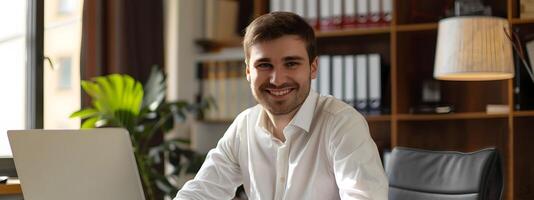 Smiling Young Corporate Professional Working Diligently at Desk with Laptop photo