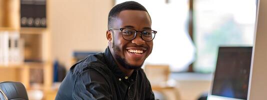 Smiling African American Program Administrator Happily Using Laptop in Modern Office Setting photo