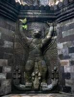A carved statue of Garudeya or Garuda clutching a multi-headed snake, located in an old temple complex in Java photo