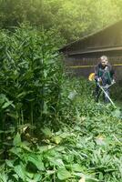 Man mows and cuts the grass with a gasoline trimmer in the garden. Mows nettle grass. vertical photo