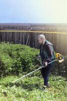 Man mows and cuts the grass with a gasoline trimmer in the garden. Mows nettle grass. side view photo