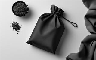 Minimalist black packaging with black sesame seeds in a bowl and scattered on a light gray background, featuring a fabric drawstring bag. photo