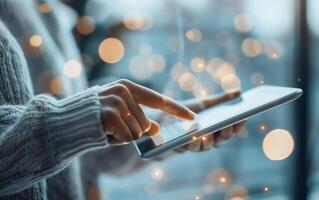 Close-up of a person's hand using a digital tablet with a bokeh background, representing technology and lifestyle in a modern environment. photo