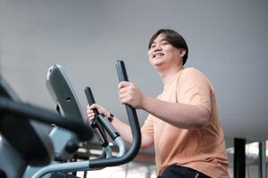 Overweight man smiling while exercising on elliptical photo