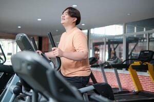 Overweight man smiling while exercising on elliptical photo