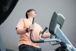 Overweight man exercising on an elliptical machine in the gym photo