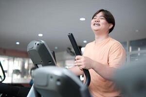 Overweight man smiling while exercising on elliptical photo