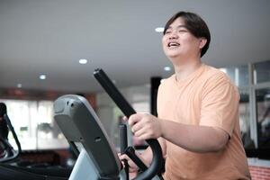 Overweight man smiling while exercising on elliptical photo