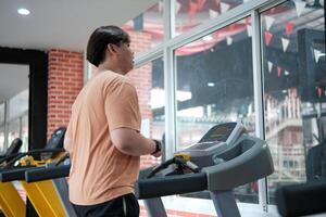Overweight man running on treadmill in gym photo