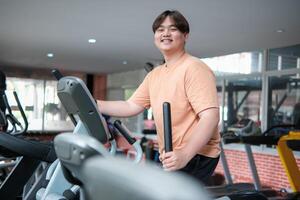 Overweight man smiling while exercising on elliptical photo
