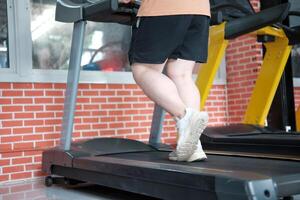 Close-up shot of an overweight man's legs walking on a treadmill in the gym. photo