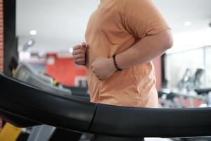 Overweight man running on treadmill in gym photo
