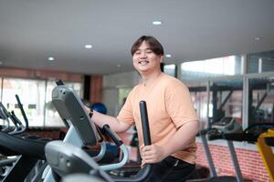 Overweight man smiling while exercising on elliptical photo