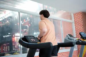 Overweight man running on treadmill in gym photo