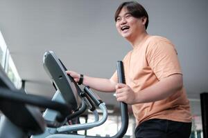Overweight man smiling while exercising on elliptical photo
