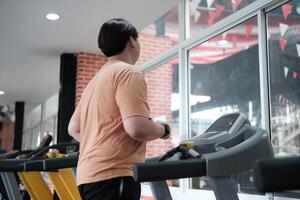 Overweight man running on treadmill in gym photo