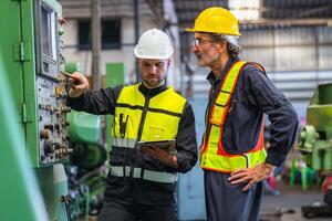 wo men in safety gear are standing next to a machine, one pointing at a button photo