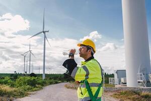 man in a yellow vest is drinking water while standing in front of a wind farm photo