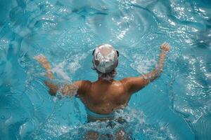 Aerial view of a woman with a swim cap swimming in the crystal clear water of a pool photo