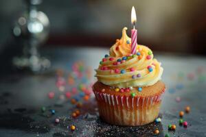 Delicious cupcake decorated with icing and sprinkles is sitting on table and lit candle is burning for birthday celebration photo