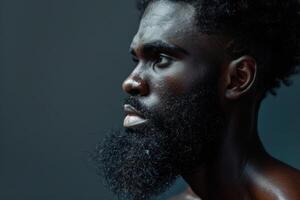 Serious black man with beard is posing on dark background in studio shot photo