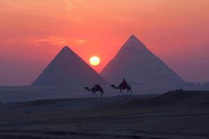 Caravan crossing the desert with ancient pyramids in background at sunset photo