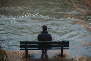 Contemplative man sitting alone on riverside bench photo