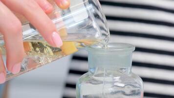 Pouring liquid into a bottle. Close up of female hands pouring liquid laundry detergent into cap on white rustic table with towels in wicker basket video