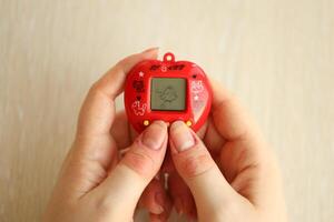 KYIV, UKRAINE - MARCH 9, 2024 Retro pet keychain game tamagotchi in red plastic case in female hands photo