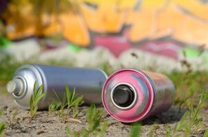 Several used spray cans with paint and caps for spraying paint under pressure on grass near the painted wall in colored graffiti photo