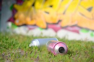 Several used spray cans with paint and caps for spraying paint under pressure on grass near the painted wall in colored graffiti photo