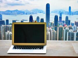 laptop in the office with a view of the city out the window - business technology concept, working on a laptop computer at office with transparency letting see a modern city landscape with skyscrapers photo