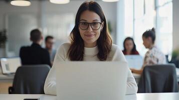 Young professional woman working on laptop in modern office setting with colleagues in the background, focused and productive photo