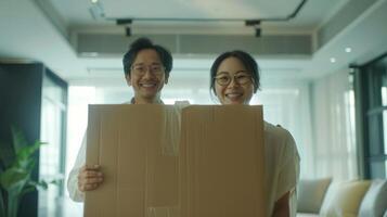 Happy asian couple holding cardboard boxes while moving into a new home, smiling joyfully in a modern living room. photo