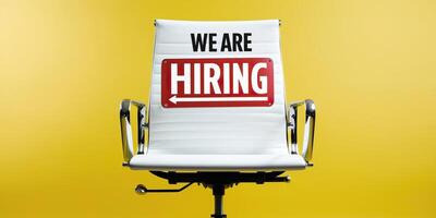 White office chair with We Are Hiring text displayed on its backrest, set against a vibrant yellow background, symbolizing job opportunities and recruitment. photo