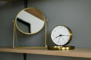 Modern Gold Analog Clock on a Shelf with Mirror photo