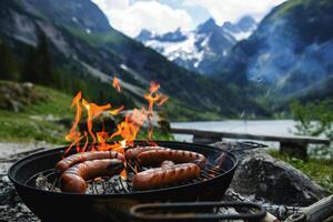 Cooking sausages on a fire with mountains in the background. camping concept photo
