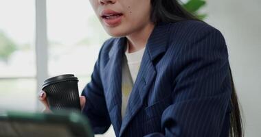Footage selective focus shot, Asian businesswoman in suit explaining work to a colleague in an online meeting via digital tablet in small coffee shop. Work from anywhere, Remote working video