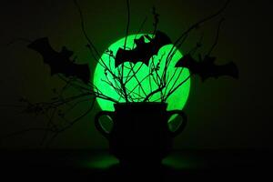Black Cauldron with dead branches and cutout bats in front of a green moon Halloween background photo