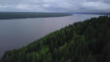 The view from the drone. Clip. A large pond over which there is a forest and a gray sky photo