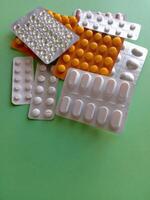 A bunch of pills are scattered on a green surface The pills are of different colors and shapes, and they appear to be in various stages of being opened. Concept of disarray and confusion photo